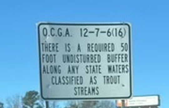 Official State of Georgia highway sign reading: O.C.G.A. 12-7-6(16) — There is a required 50 foot undisturbed buffer along any state waters classified as trout streams